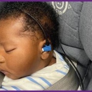 A young child is being tested with a black and blue device placed in their ear to check their response to sound.